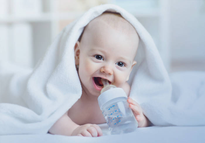 Elisabethen Quelle Babynahrung Baby liegt unter einer Decke und trinkt aus einer Babyflasche.