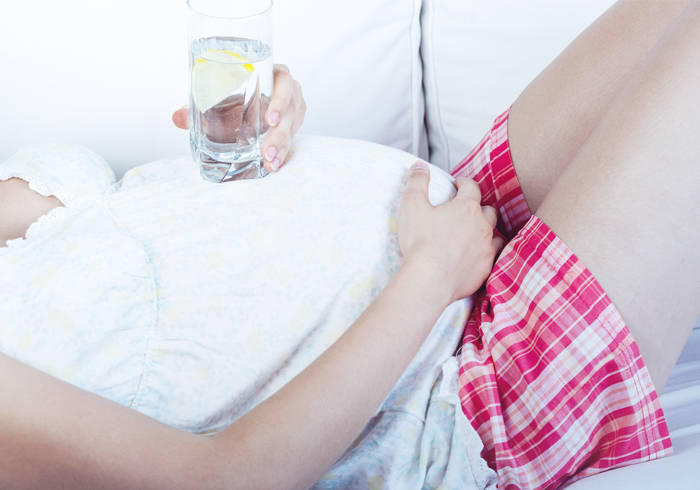 Elisabethen Quelle Schwangerschaft Schwangere Frau liegt auf dem Rücken und hält ihren Bauch, auf dem sie ein Glas Wasser abstützt.